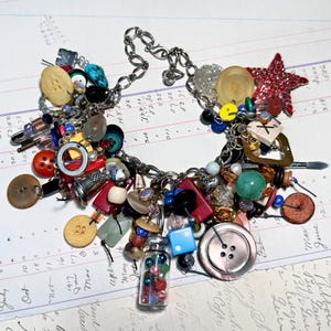 May include: A quirky charm necklace with a collection of colourful beads, buttons, and trinkets. The necklace includes a small glass vial filled with colourful beads, a red glitter star, and a large mother-of-pearl button. The chain is silver-toned.