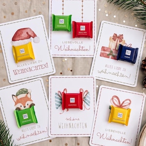 Op de afbeelding: Vijf rechthoekige witte kaarten met aquarelillustraties van kerstthema's, elk bevestigd met een klein Ritter Sport chocoladevierkantje. De tekst bevat 'ALLES LIEBE ZU WEIHNACHTEN!', 'LIEBEVOLLE Weihnachten!' en 'sch&ouml;ne WEIHNACHTEN'.