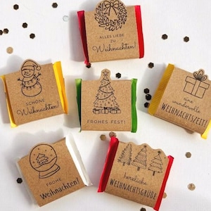 Op de afbeelding: Zes kleine rechthoekige chocoladerepen verpakt in bruin kraftpapier met feestelijke zwarte inktillustraties en Duitse kerstteksten. Elke wikkel heeft unieke ontwerpen zoals een sneeuwpop, kerstboom, krans, cadeau, sneeuwbol en een bos.