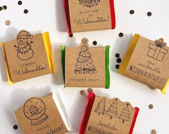 May include: Six small rectangular chocolate bars wrapped in brown kraft paper with festive black ink illustrations and German holiday text. Each wrapper features unique designs like a snowman, Christmas tree, wreath, gift, snow globe, and forest.