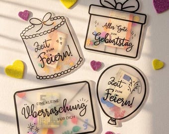 Könnte beinhalten: Vier transparente Acryl-Geschenkhalter mit schwarzen Linienzeichnungen, darunter ein Geschenkpaket, ein Luftballon und ein Umschlag. Die Halter enthalten buntes Konfetti und Geldscheine. Der Text lautet Zeit zum Feiern, Alles Gute zum Geburtstag und Eine kleine Überraschung für dich. Kleine glitzernde Herzen in Gelb und Lila sind verstreut.