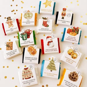 Puede incluir: Un conjunto de doce tarjetas rectangulares para calendario de adviento con ilustraciones en acuarela de iconos navideños como un muñeco de nieve, un cascanueces y un árbol de Navidad, cada una con un círculo numerado y texto en alemán.