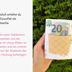 May include: A white paper card featuring a printed ice cream cone pocket design. A twenty euro banknote is tucked into the pocket. The card has a light pattern of tropical leaves and beach items. The text reads: Zus&auml;tzlich erh&auml;ltst du eine Eiswaffel als Geldtasche. Einfach einen Geldschein hineinstecken und die Tasche mit etwas Kleber an den Seiten und am unteren Rand auf der R&uuml;ckseite der Duplo-Packung befestigen.