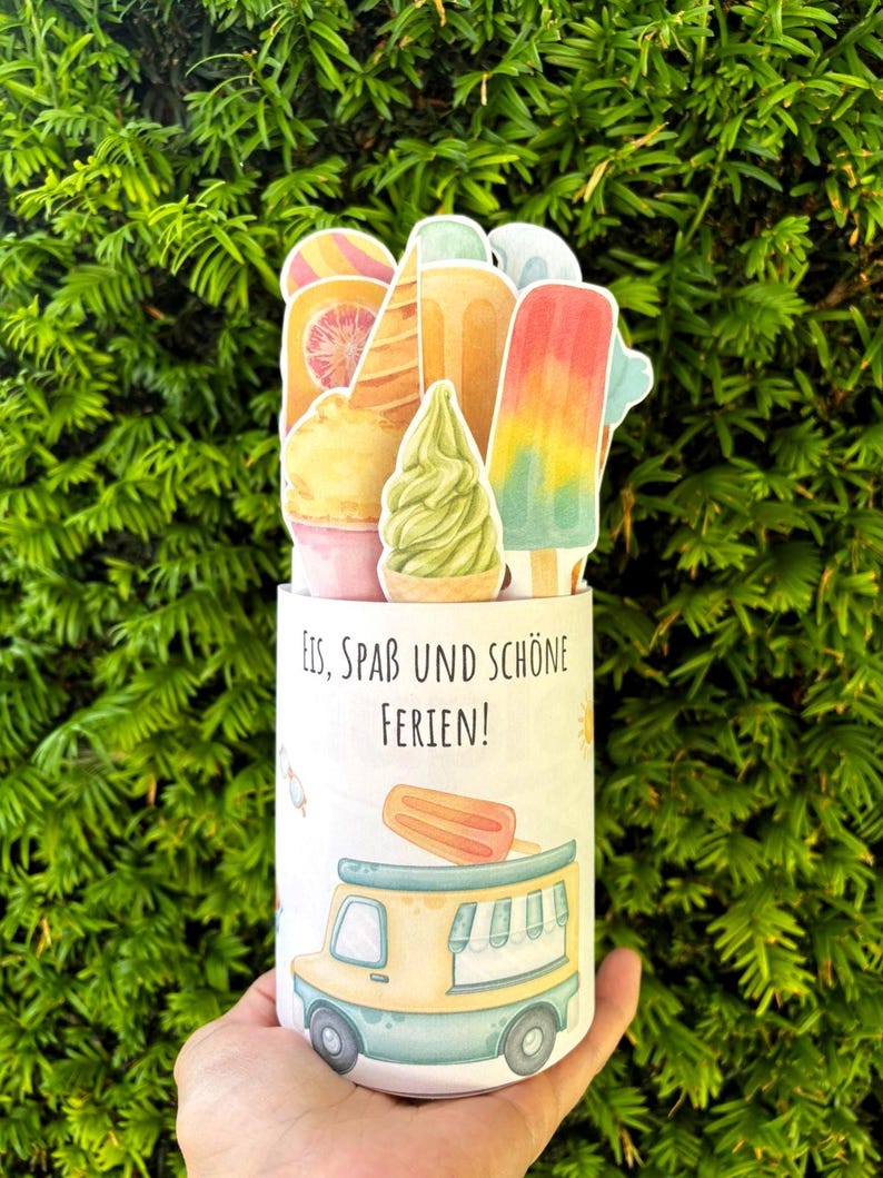 May include: A cylindrical container featuring a graphic of an ice cream truck and the German text Eis, Spa&szlig; und Sch&ouml;ne Ferien. The top is decorated with various die-cut paper illustrations of colorful ice cream cones, popsicles, and sorbet.