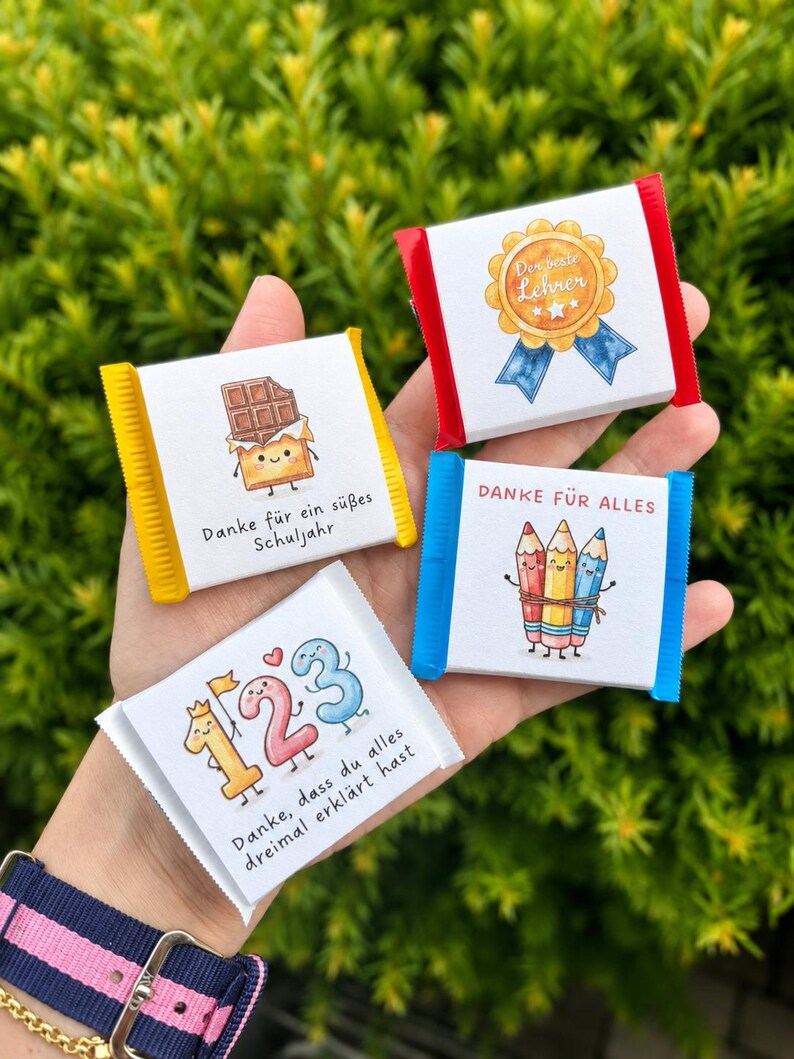 Op de afbeelding: Vier kleine rechthoekige chocoladerepen met witte wikkels voorzien van kleurrijke illustraties en Duitse tekst. De afbeeldingen tonen een chocoladereep, een gouden medaille, drie kleurpotloden en de cijfers 1, 2 en 3 met een kroontje.