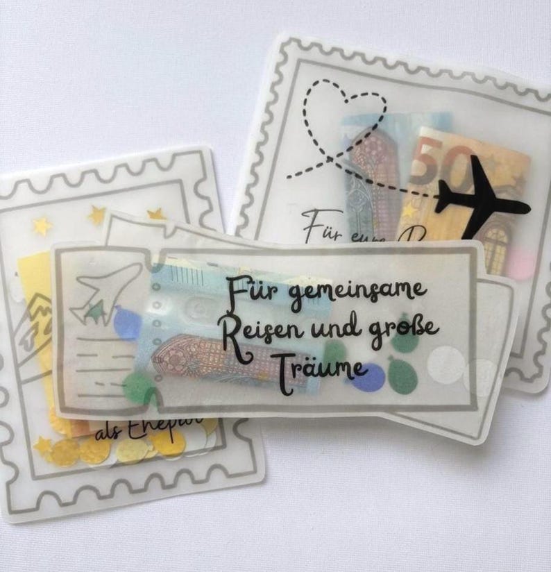 May include: Three translucent envelopes shaped like postage stamps and a ticket, containing paper currency and colorful confetti. The ticket features the black text "F&uuml;r gemeinsame Reisen und gro&szlig;e Tr&auml;ume" and a small airplane icon, while others show a heart and plane.