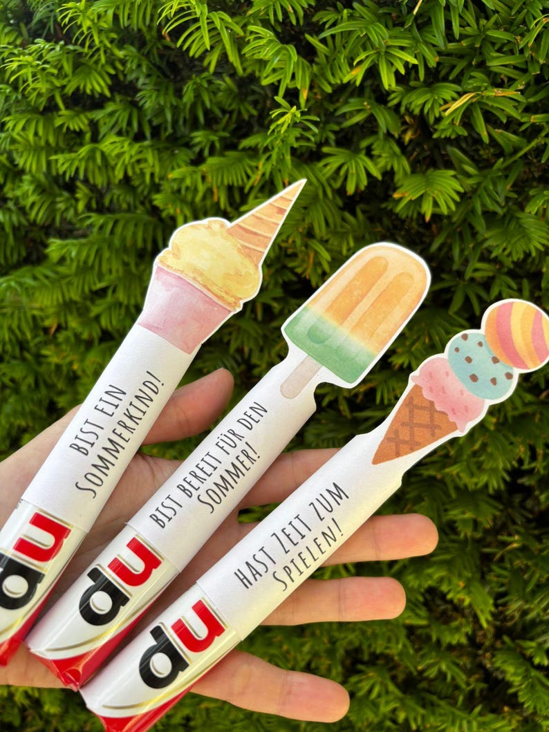 May include: Three white cylindrical tubes with red and black branding at the base, each topped with a different ice cream illustration. The text reads BIST EIN SOMMERKIND!, BIST BEREIT F&Uuml;R DEN SOMMER!, and HAST ZEIT ZUM SPIELEN! in black lettering.