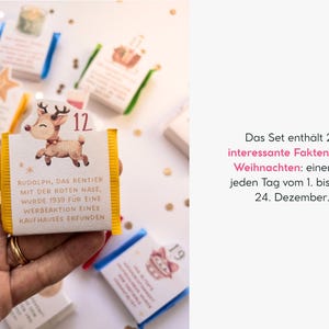 May include: A small rectangular card with a yellow border featuring a cartoon reindeer and the number 12. The text reads: Rudolph, das Rentier mit der roten Nase, wurde 1939 f&uuml;r eine Werbeaktion eines Kaufhauses erfunden. Part of a 24-piece set.