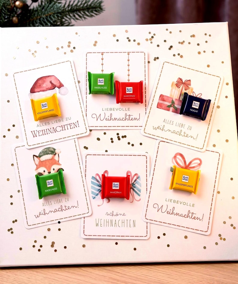 Op de afbeelding: Zes rechthoekige kaarten met gouden confetti-accenten, elk voorzien van een kleine Ritter Sport chocoladereep. De kaarten tonen aquarelillustraties van kerstthema's en Duitse tekst, waaronder Alles Liebe zu Weihnachten en Sch&ouml;ne Weihnachten.