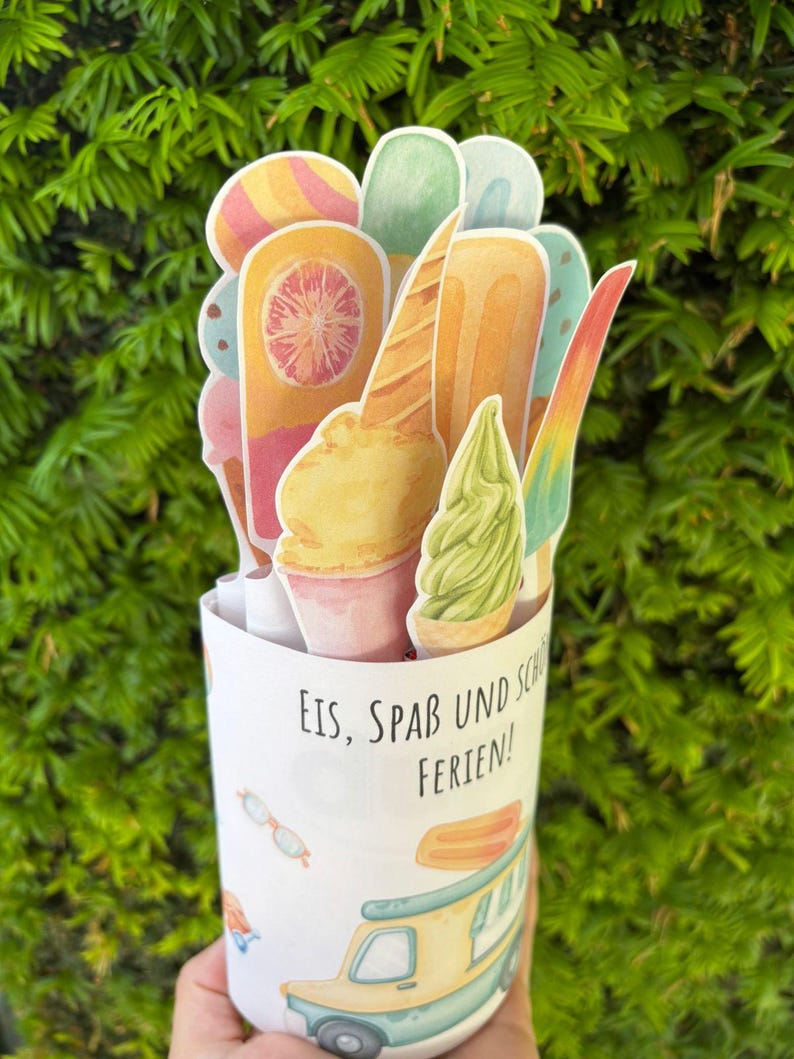 May include: A cylindrical paper container featuring a light blue ice cream truck illustration and the text "EIS, SPA&szlig; UND SCH&Ouml;NE FERIEN!" filled with various die-cut paper ice cream treats including popsicles, cones, and soft serve.