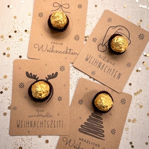 Könnte beinhalten: Vier rechteckige Karten aus Kraftpapier, jede mit einer goldfolierten Schokoladentrüffel in einer dunkelbraunen Papierform. Die Karten zeigen schwarze Illustrationen von Weihnachtsmotiven wie Baumschmuck, Weihnachtsmütze, Rentiergeweih und Tannenbaum.