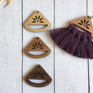 May include: Wooden earrings in three shades of brown, featuring a laser-cut floral design and a semi-circular bottom. A pair of earrings with a purple tassel is also visible. The earrings are displayed on a white wooden surface.