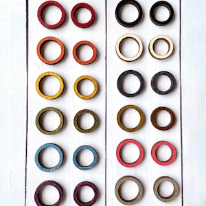 May include: A set of 20 wooden rings in various colors, including red, orange, yellow, green, blue, purple, and gray. The rings are arranged in two rows of ten, with each row featuring a different color scheme.