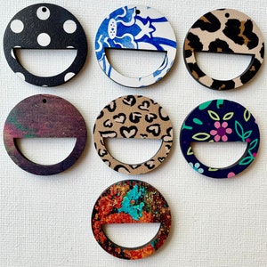 May include: Set of eight round wooden ornaments with different patterns. The ornaments are painted with various designs, including polka dots, floral patterns, and abstract designs. Each ornament has a hole at the top for hanging.