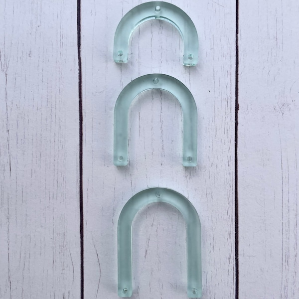 Op de afbeelding: Drie frosted acryl bogen in verschillende maten, verticaal gerangschikt op een witte houten achtergrond.