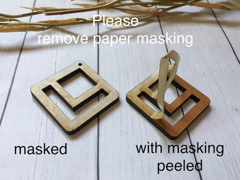May include: Two wooden squares with a geometric design. The square on the left has a paper masking covering the design. The square on the right has the paper masking peeled off, revealing the natural wood underneath. The text "Please remove paper masking" is written above the squares. The text "masked" is written below the square on the left. The text "with masking peeled" is written below the square on the right.
