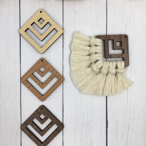 May include: Three wooden diamond-shaped earrings with a geometric pattern cut out. The earrings are in different shades of brown. A white macrame tassel hangs below a wooden square earring with a geometric pattern cut out.