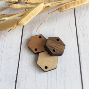 May include: Three wooden hexagon shapes in different shades of brown. The shapes have two holes each.