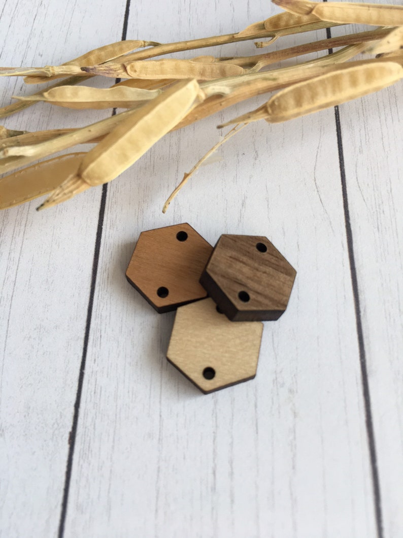 May include: Three wooden hexagon shapes in different shades of brown. The shapes have two holes each.