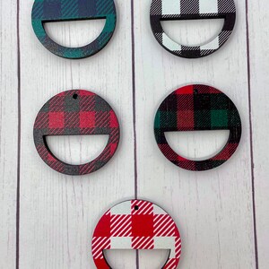 May include: Five round wooden ornaments with a cut-out shape in the bottom half. The ornaments are decorated with different plaid patterns in red, green, black, and white.