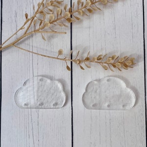 May include: Two clear acrylic cloud-shaped ornaments. The clouds are smooth and have a slightly frosted appearance.