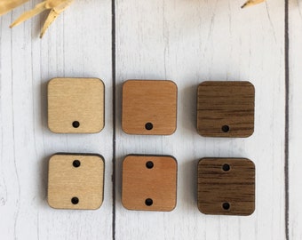Peut inclure: Six étiquettes carrées en bois avec des trous. Trois étiquettes sont brun clair, trois étiquettes sont brun foncé. Les étiquettes sont disposées en deux rangées de trois.