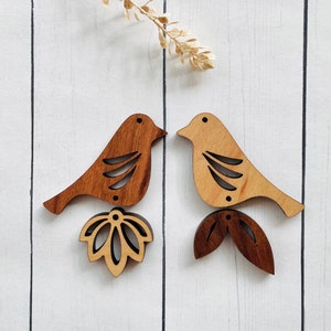 May include: Two wooden bird ornaments with intricate cutouts. The birds are facing each other and have a brown and natural wood finish. Each bird has a flower or leaf design attached to the bottom.