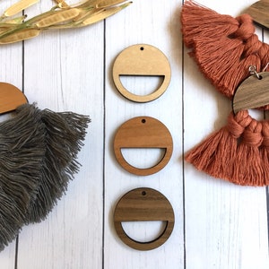 May include: Wooden earrings with macrame fringe in gray and terracotta colors. The earrings have a half-circle wooden top and a circular wooden base with a semi-circular cutout. The earrings are displayed on a white wooden surface.