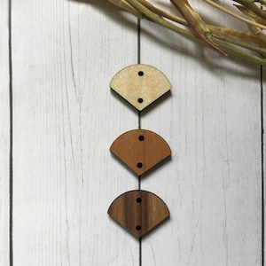 May include: Three wooden buttons in the shape of a fan. The buttons are in different shades of brown, from light to dark.