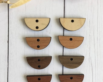 May include: Eight wooden half-circle buttons with two holes each. The buttons are in three different shades of brown, with the top two buttons being the lightest shade and the bottom two buttons being the darkest shade.