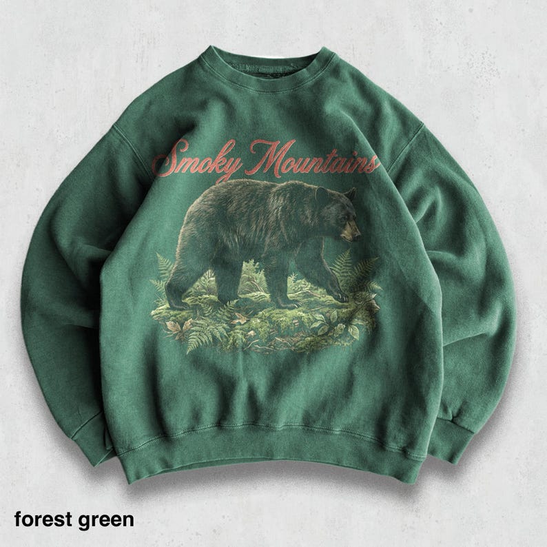 May include: Forest green sweatshirt featuring a graphic of a black bear walking through ferns, with "Smoky Mountains" in a cursive font above the bear. The sweatshirt is a solid forest green color.