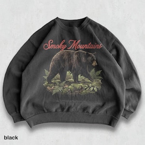 May include: Black sweatshirt featuring a graphic of a bear walking through ferns, with the text "Smoky Mountains" in red script above. The word "black" is printed at the bottom of the sweatshirt.