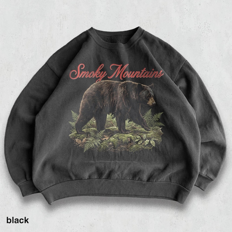 May include: Black sweatshirt featuring a graphic of a bear walking through ferns, with the text "Smoky Mountains" in red script above. The word "black" is printed at the bottom of the sweatshirt.