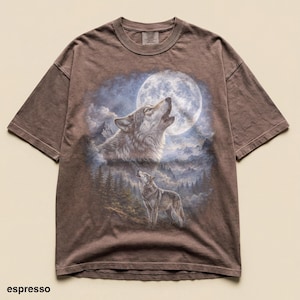 May include: Espresso-colored t-shirt featuring a detailed graphic of two wolves howling at a full moon in a forest setting. The design includes a large, bright moon and a mountainous landscape. The shirt has short sleeves and a crew neck.