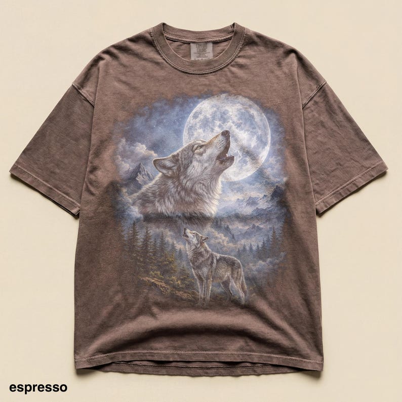 May include: Espresso-colored t-shirt featuring a detailed graphic of two wolves howling at a full moon in a forest setting. The design includes a large, bright moon and a mountainous landscape. The shirt has short sleeves and a crew neck.