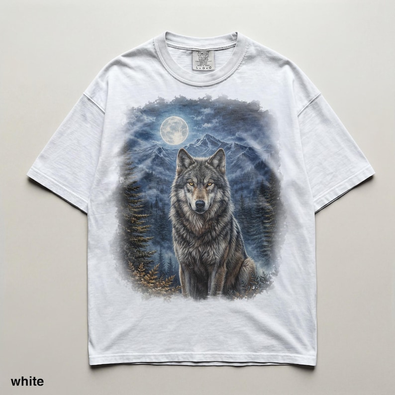 May include: White t-shirt featuring a detailed illustration of a wolf in a forest setting under a full moon. The wolf has gray and brown fur, with mountains and trees in the background. The text "TIMELESS COLORS" is visible on the upper right.