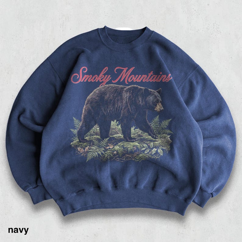 May include: Navy blue sweatshirt featuring a black bear walking through a forest scene. The words "Smoky Mountains" are arched across the top in pink script. The word "navy" is printed at the bottom of the sweatshirt.