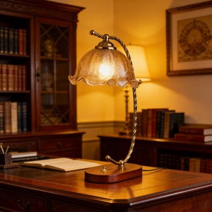 Pode incluir: Uma luminária de mesa em estilo vintage com uma cúpula de vidro âmbar texturizado e uma base de latão decorativa. A luminária possui um braço de metal torcido e fica sobre uma base de madeira. A luminária está acesa, iluminando o ambiente.