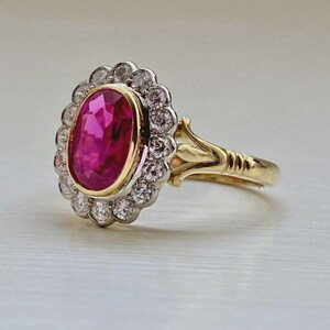 Puede incluir: Un anillo de oro con una gran gema rosa brillante de corte ovalado en el centro, rodeada por un halo de gemas claras más pequeñas. La banda del anillo es dorada, con detalles intrincados cerca del engaste.