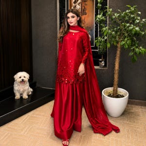 May include: A vibrant red long-sleeved tunic and matching floor-length skirt set. The tunic features intricate red sequin embellishments concentrated at the hemline and scattered across the front. A coordinating red scarf drapes over the shoulder.