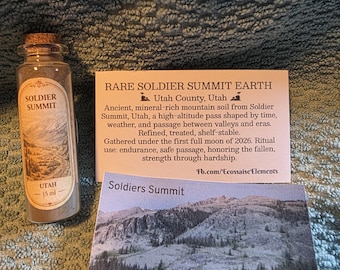 Può includere: Una piccola bottiglia di vetro con l'etichetta "SOLDIER SUMMIT UTAH 15 ml" con un tappo di sughero, contenente terra. È presente anche una scheda con il testo "RARE SOLDIER SUMMIT EARTH" e una foto di un paesaggio montano.