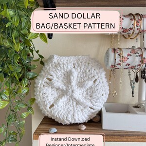 Op de afbeelding: Een wit, gehaakt zanddollar tas- of mandpatroon. De tas is rond met een textuurontwerp en openwerkdetails. Tekst op de afbeelding luidt "Sand Dollar Bag/Basket Pattern" en "Instant Download Beginner/Intermediate".