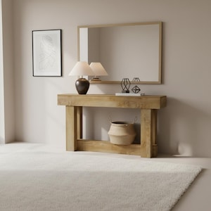 Puede incluir: Una consola de madera clara con un espejo rectangular y dos lámparas. Una cesta tejida se encuentra en el estante inferior. Objetos decorativos y una obra de arte abstracta enmarcada completan la decoración. La alfombra es blanca.