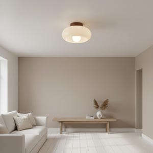 Könnte beinhalten: Eine moderne Deckenleuchte mit rundem, mattiertem Glasschirm und dunklem Holzsockel. Das Licht ist eingeschaltet und erhellt den Raum. Die Leuchte ist an einer weißen Decke montiert.