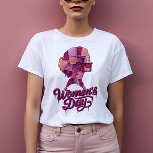 Puede incluir: Camiseta blanca con un gráfico de la silueta de una mujer hecha de cuadrados de patchwork rosas y morados. Las palabras "Women's Day" están escritas en una fuente goteante debajo.