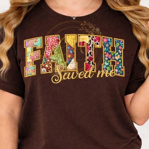 Puede incluir: Una camiseta marrón con la palabra "FAITH" en un diseño de patchwork con telas florales y estampadas. Debajo de la palabra "FAITH" está la frase "Saved me" en una fuente cursiva. La camiseta tiene cuello redondo.