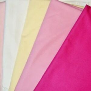 This is a photo of fabrics that the bonnets are made with. They are on an angle going across the photo like a fan. There is solid light pink, white, yellow, medium pink, and bright pink.