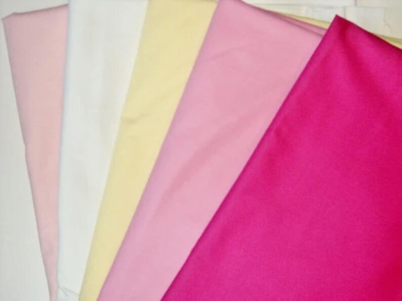 This is a photo of fabrics that the bonnets are made with. They are on an angle going across the photo like a fan. There is solid light pink, white, yellow, medium pink, and bright pink.