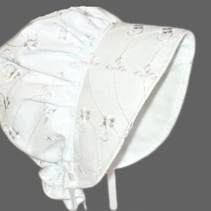 Peut inclure: Un bonnet blanc avec un bord festonné et un motif floral délicat. Le bonnet est fait d'un tissu doux et léger et a un design simple.