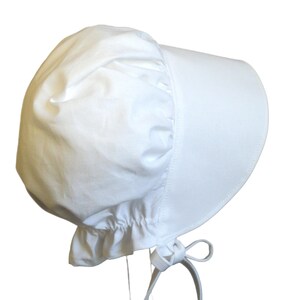 White prairie bonnet with wide brim facing right. Some of the bonnet back is showing. The side-back is puffy and gathered onto the brim. It it has a gathered ruffle at the bottom back. A white bow is tied under the hat with ties hanging down.